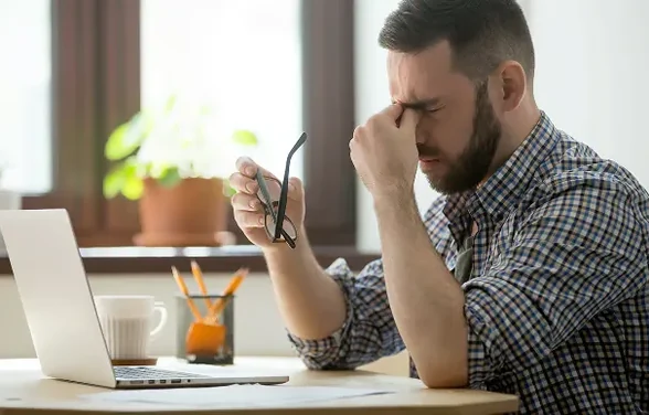 Müder Mann vor seinem Laptop, die Brille in der Hand